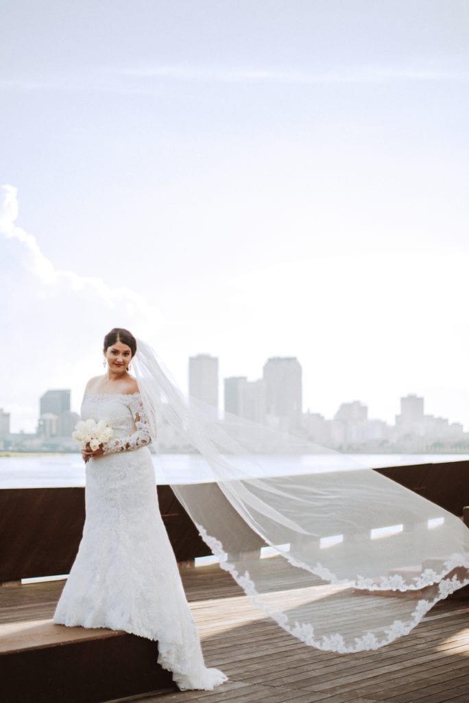 bride standing tall with her veil flowing in the wind and the sky line of new orleans as her backdrop these are stunning bridal portraits at crescent park