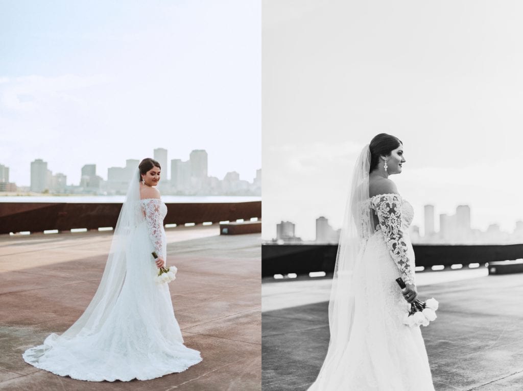 bride standing in full length dress with lace sleeves looking over her shoulder with the sky line of new orleans as her backdrop these are stunning bridal portraits at crescent park