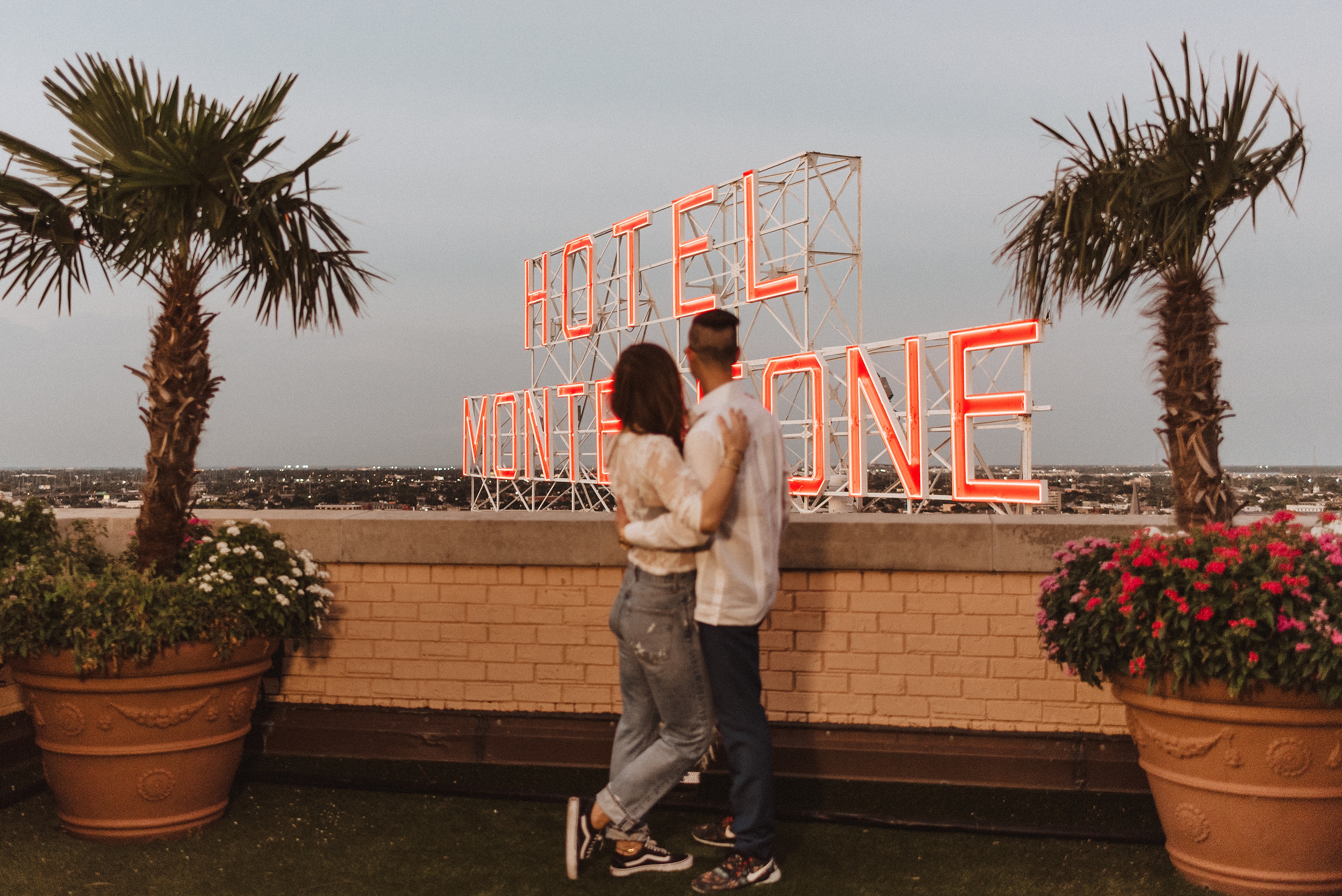 couple stands in front of the Hotel Monteleone sign taking in the sunset after their rooftop proposal 