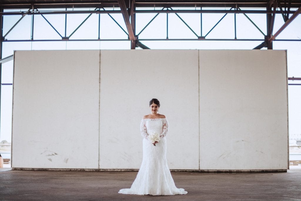 bride standing in a full length dress in front of a white wall looking beautiful for her bridal portraits in crescent park new orleans